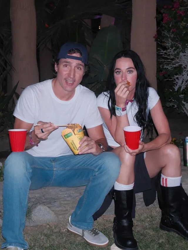 Two people sit on a curb outdoors at night, holding red cups and eating food.